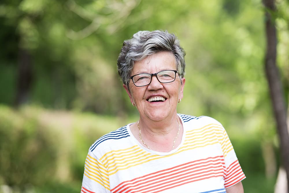 A senior woman with glasses standing outside and smiling